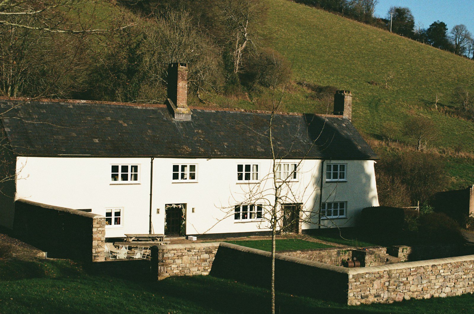 White farmhouse with stone walls and green hills.