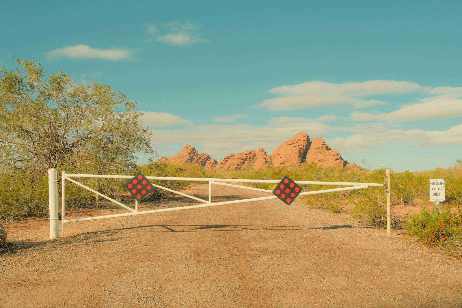 White gate blocks dirt road leading to rocky desert mountains