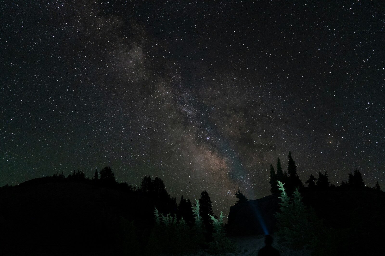 Stunning milky way galaxy over dark forest with person's headlamp.