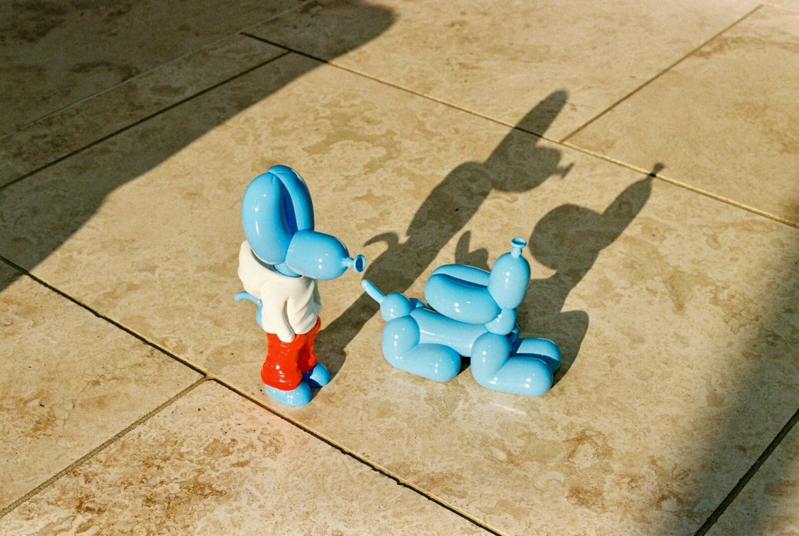 Blue balloon-dog sculptures meet nose to nose on stone tiles