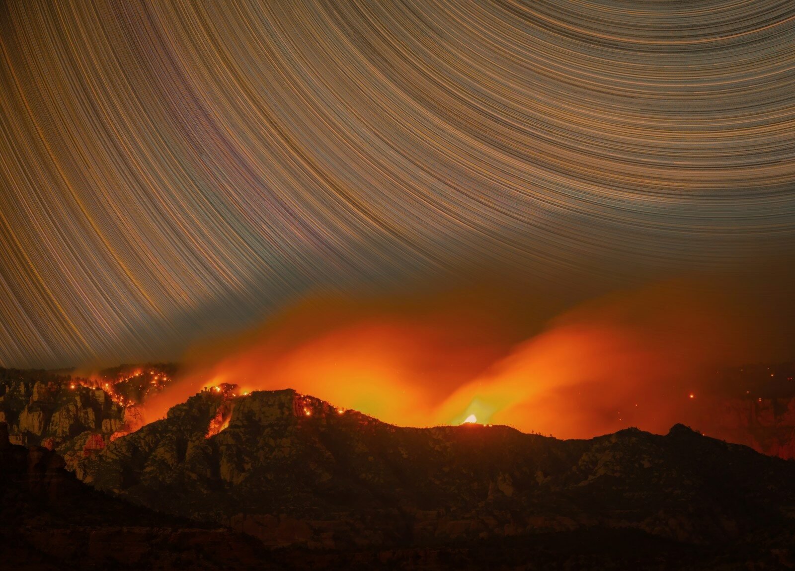 Mountains ablaze with fire under a sky of star trails.