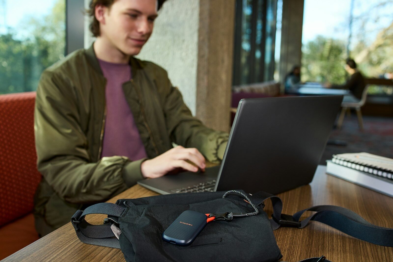 Young man uses laptop, portable storage device on table.